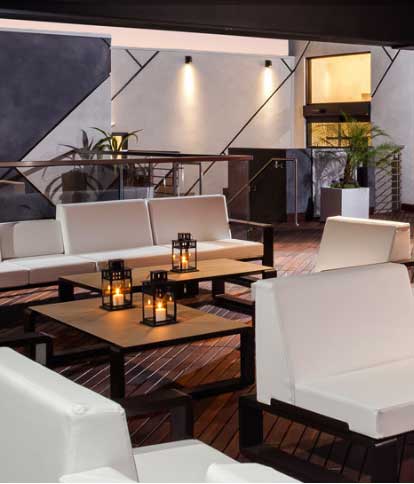 A stylish outdoor lounge area with white furniture, wooden floors, and warm candlelight.