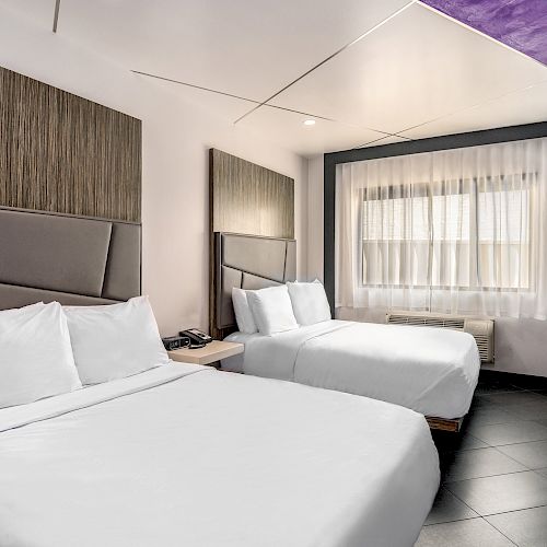 A hotel room with two beds, a window with curtains, and a tiled floor.