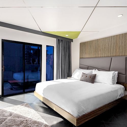 A modern hotel room with a large bed, sliding glass doors, and a city view.