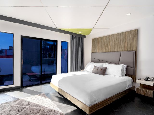 A modern hotel room with a large bed, sliding glass doors, and a modern headboard.