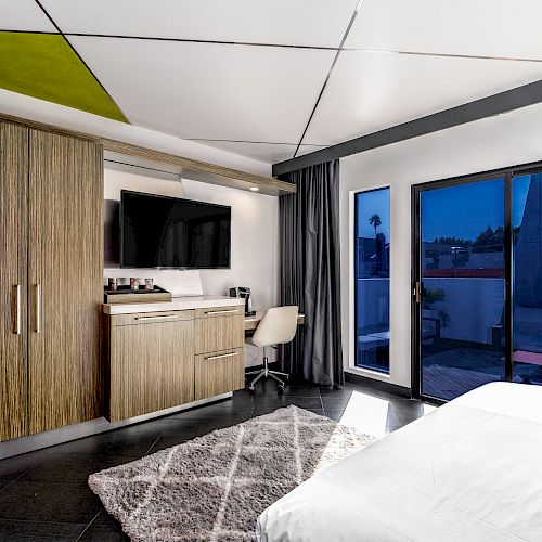A modern hotel room with a bed, desk, TV, and balcony