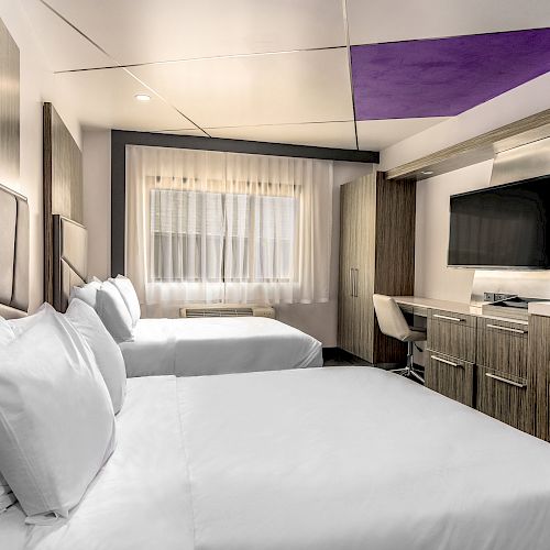A hotel room with two beds, a TV, and a desk.