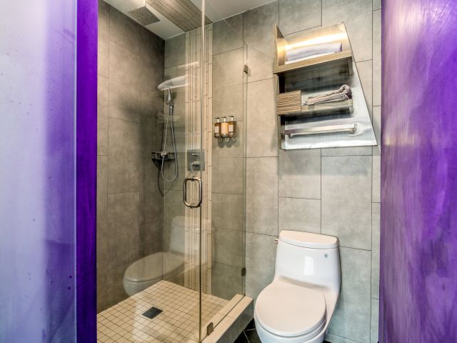 A bathroom with a glass-enclosed shower, white toilet, gray tiles, and a purple wall.