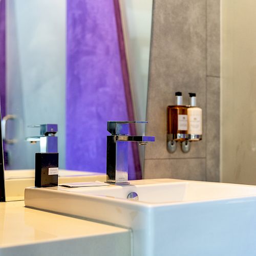 A modern bathroom sink with a mirror and shampoo bottles