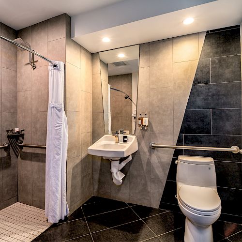 A clean and modern bathroom with tiled walls, a separate shower, wall-mounted sink, and toilet.