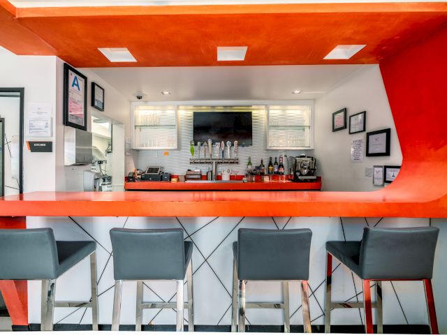 A modern bar with an orange counter and gray stools