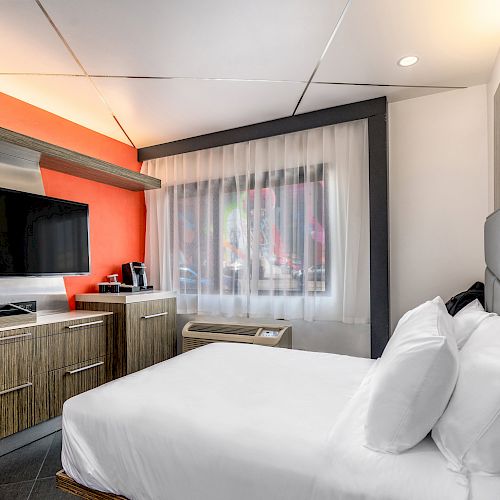 A hotel room with a bed, TV, coffee maker, and window.