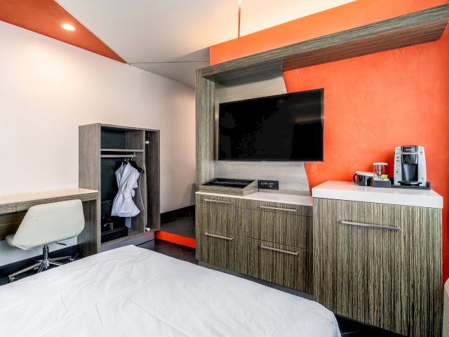 A wide view of a hotel room with a bed, desk, closet, TV, and coffee maker.