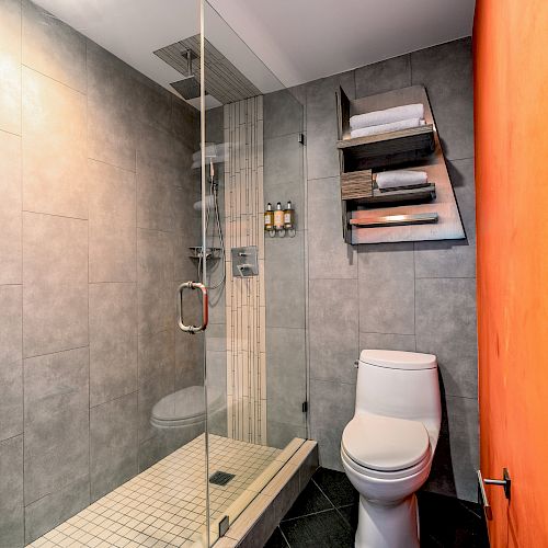 A modern bathroom with a glass-enclosed shower, toilet, and tiled walls and floor.