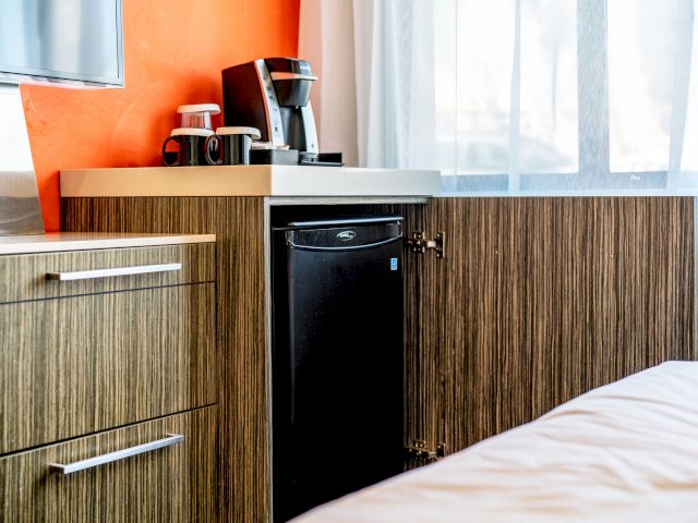 A hotel room with a coffee maker, mini fridge, and bed