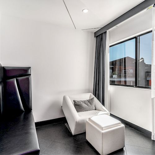 A modern hotel room with a black leather bed, white armchair, and ottoman.