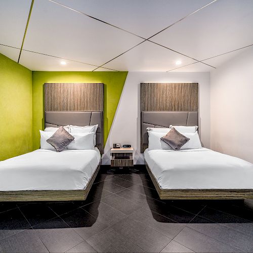 A hotel room with two beds, a nightstand, and a green accent wall.