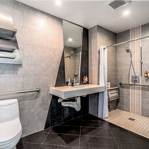 A modern bathroom with a floating sink, large mirror, shower, and toilet.