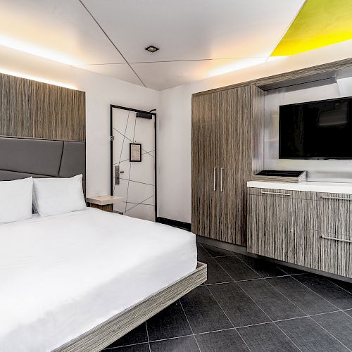 A modern hotel room with a white bed, wooden furniture, and a flat screen TV.
