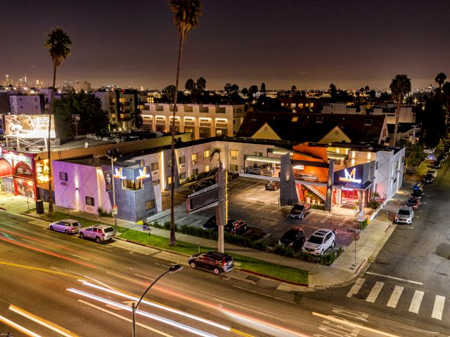 A nighttime aerial view of a hotel exterior with a parking lot and city skyline in the background.