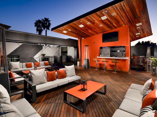 A stylish outdoor lounge area with an orange accent wall, wooden ceiling, and comfortable seating.