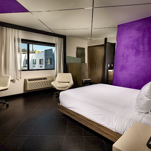 A modern hotel room with a large bed, chair, and window