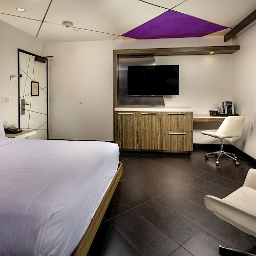 A wide view of a hotel room with a bed, desk, TV, and chair