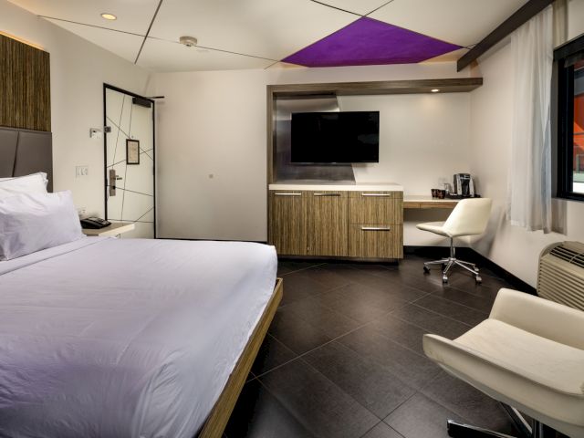 A modern hotel room with a large bed, flat-screen TV, desk area, and comfortable seating.