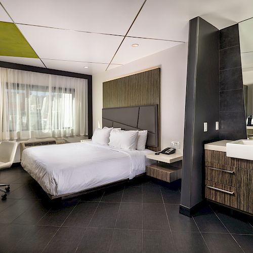 A modern hotel room with a large bed, window, desk area, and modern furniture.