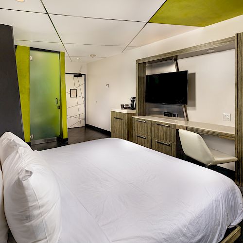 A modern hotel room with a large bed, desk, TV, and chair.