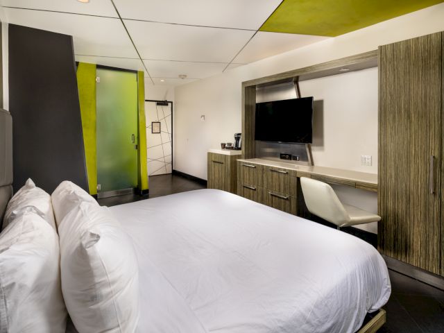 A modern hotel room with a large bed, desk, TV, and closet.