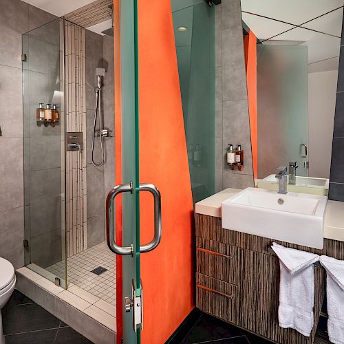 A modern bathroom with a glass shower door, orange accent wall, and wooden cabinet.