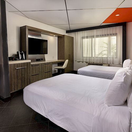 A hotel room with two beds, a desk, and a window.