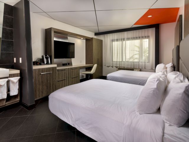 A hotel room with two queen beds, a desk, TV, and coffee maker.