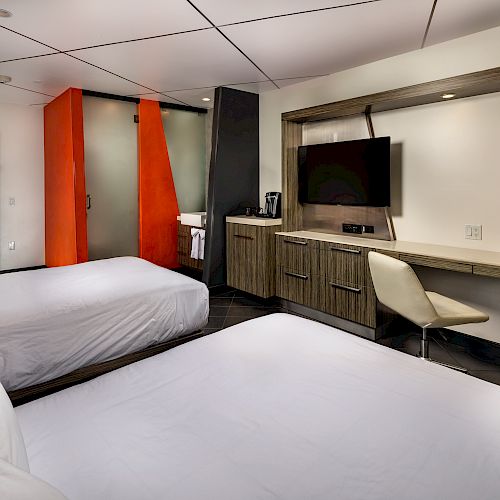 A hotel room with two beds, a desk, a TV, and a cabinet.