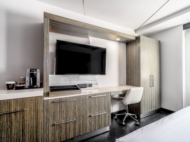 A modern hotel room with a desk, TV, coffee maker, and bed.