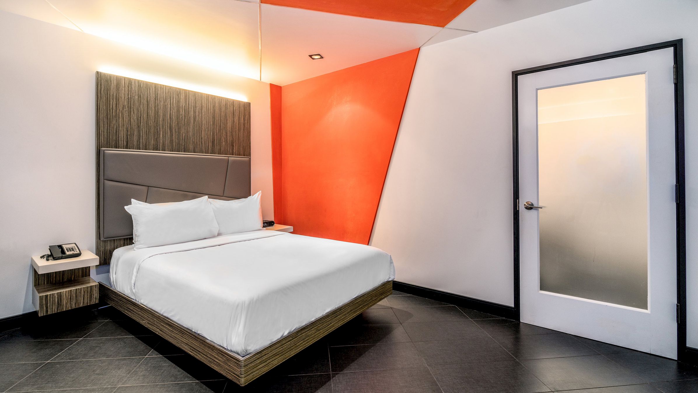 A hotel room with a bed, nightstand, and door