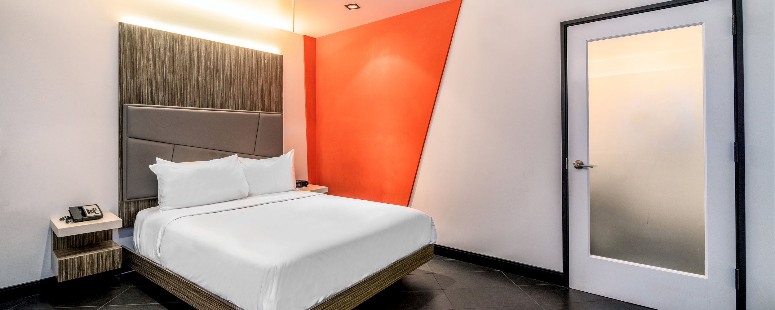 A hotel room with a bed, nightstand, and door