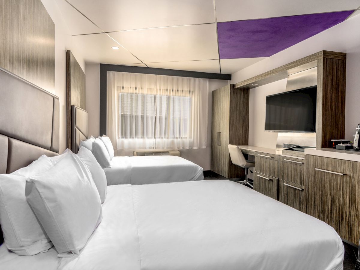 A hotel room with two beds, a desk, a TV, and a window