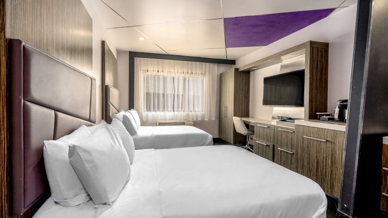 A hotel room with two double beds, a desk, and a TV