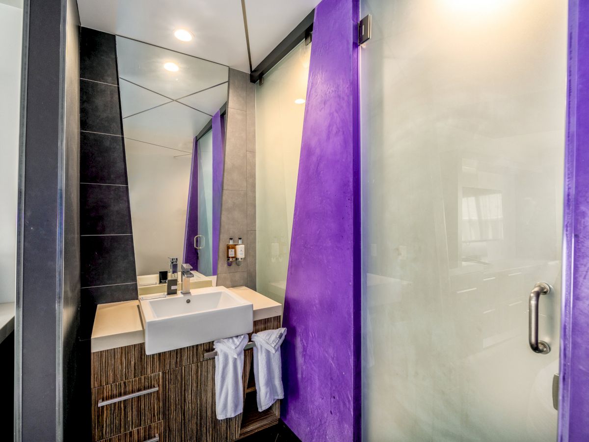 A modern bathroom with a purple accent wall, a glass shower door, and a modern sink.