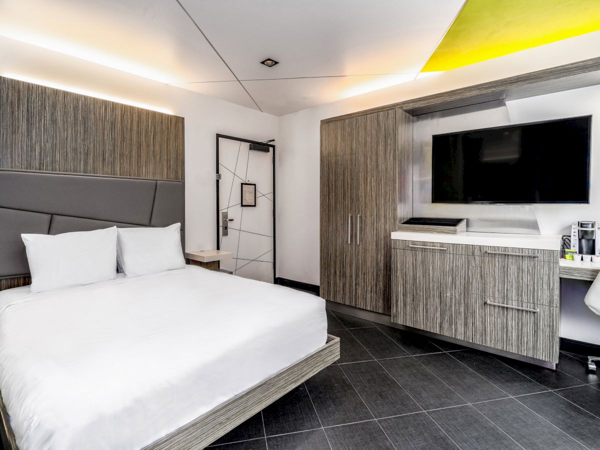 A modern hotel room with a large bed, TV, and cabinet.