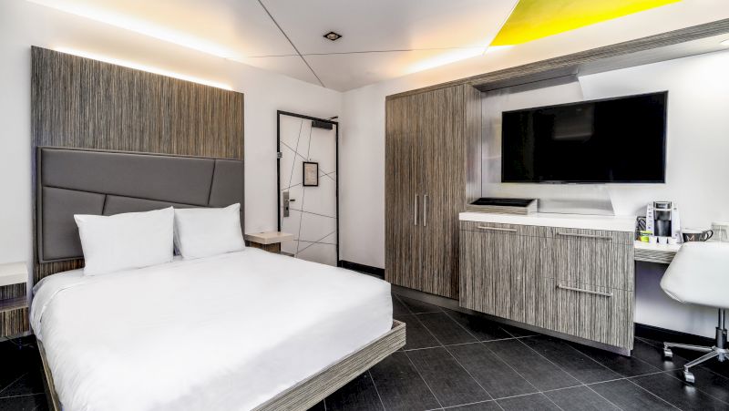 A wide-angle view of a hotel room with a bed, desk, TV, and cabinet.
