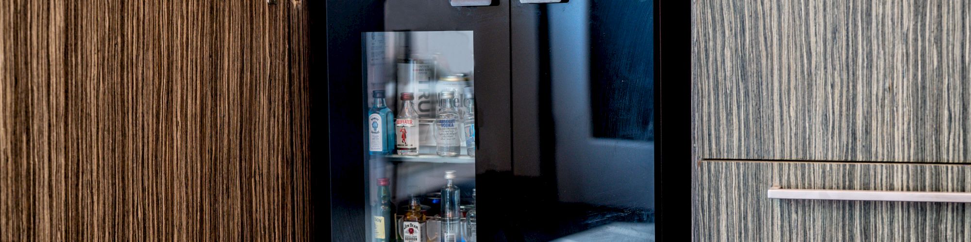 A mini bar with a glass door showing various liquor bottles inside.