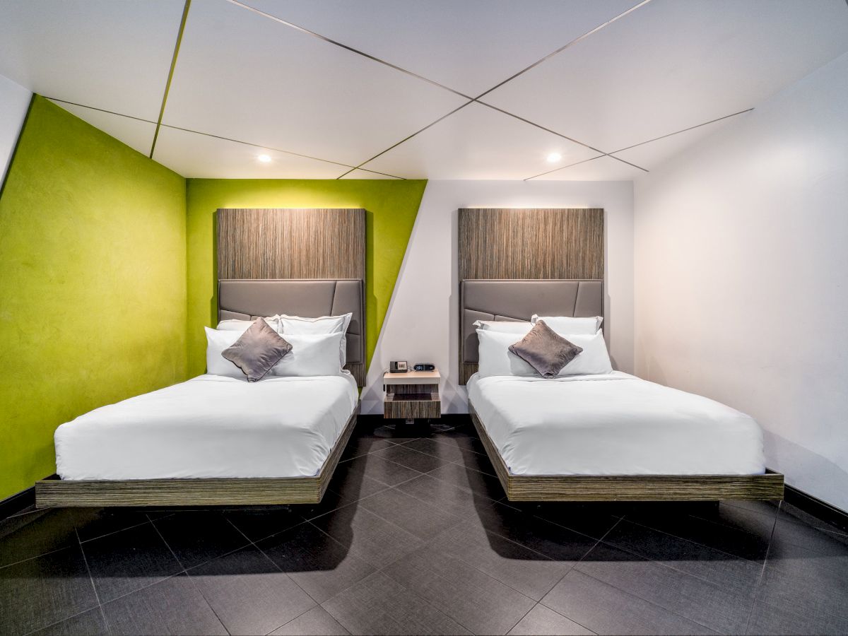 A hotel room with two twin beds, green accent wall, wood headboards, white linens, and black tile floor.