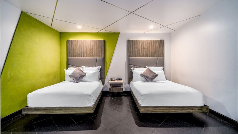 A hotel room with two beds, a green accent wall, and wooden headboards.